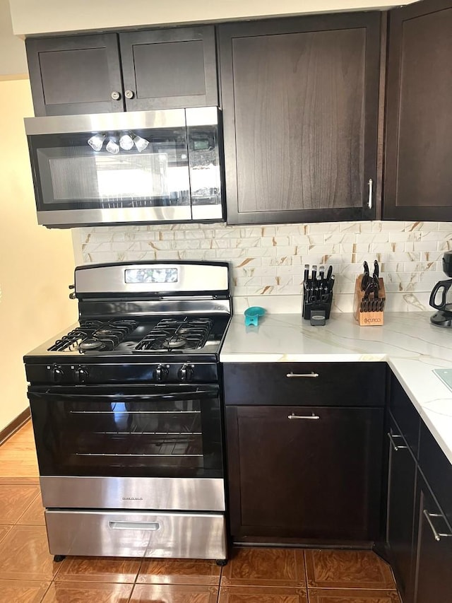 kitchen with tasteful backsplash, light stone counters, dark brown cabinets, and range with gas cooktop