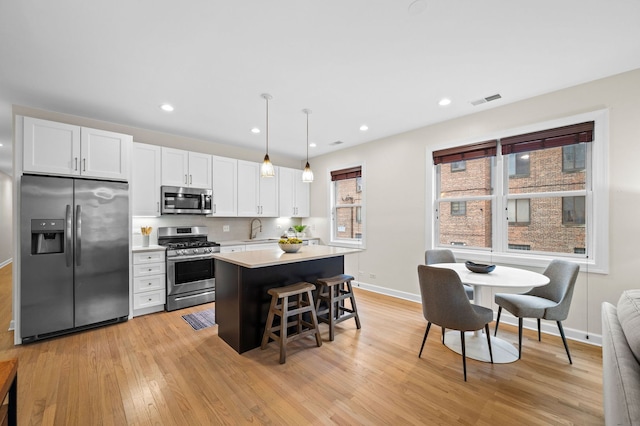 kitchen with sink, decorative light fixtures, appliances with stainless steel finishes, a kitchen breakfast bar, and white cabinets