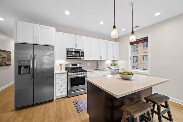 kitchen with sink, appliances with stainless steel finishes, white cabinetry, a kitchen breakfast bar, and decorative light fixtures