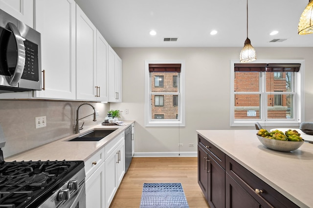 kitchen with pendant lighting, sink, stainless steel appliances, tasteful backsplash, and white cabinets