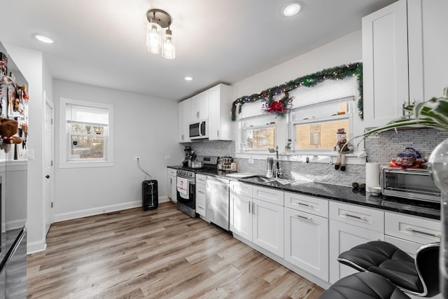 kitchen with stainless steel appliances, decorative backsplash, dark stone counters, white cabinets, and sink