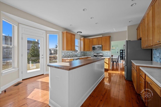 kitchen with appliances with stainless steel finishes, sink, light hardwood / wood-style floors, and backsplash