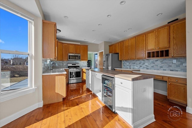 kitchen featuring appliances with stainless steel finishes, a kitchen island, beverage cooler, light hardwood / wood-style floors, and decorative backsplash