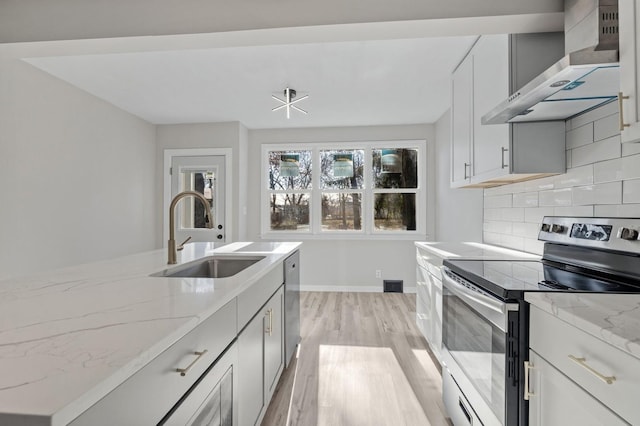 kitchen featuring tasteful backsplash, wall chimney range hood, sink, appliances with stainless steel finishes, and light stone countertops