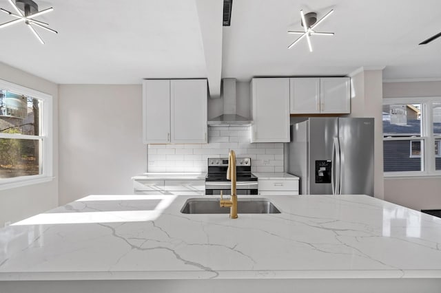 kitchen featuring white cabinets, wall chimney range hood, stainless steel appliances, backsplash, and light stone counters