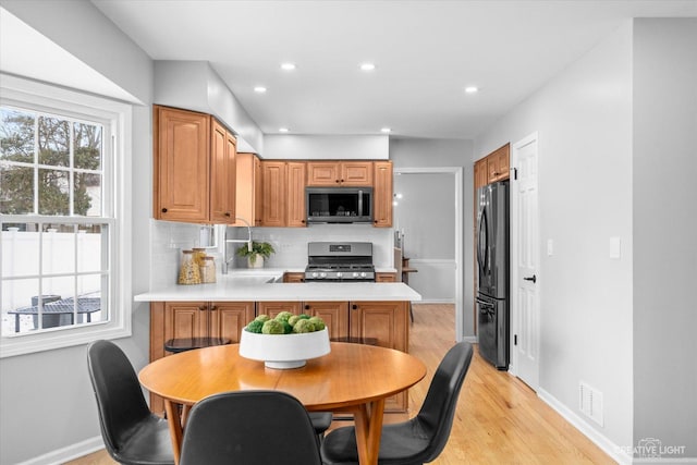 kitchen featuring kitchen peninsula, tasteful backsplash, light hardwood / wood-style flooring, and stainless steel appliances