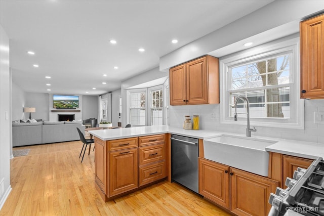 kitchen featuring kitchen peninsula, stainless steel dishwasher, sink, light wood-type flooring, and tasteful backsplash