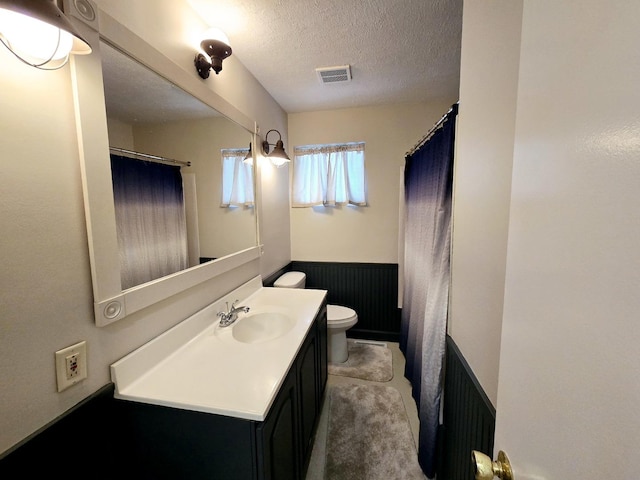 full bathroom with visible vents, toilet, a textured ceiling, wainscoting, and vanity