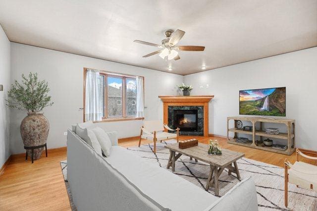 living room featuring a premium fireplace, ceiling fan, and light wood-type flooring