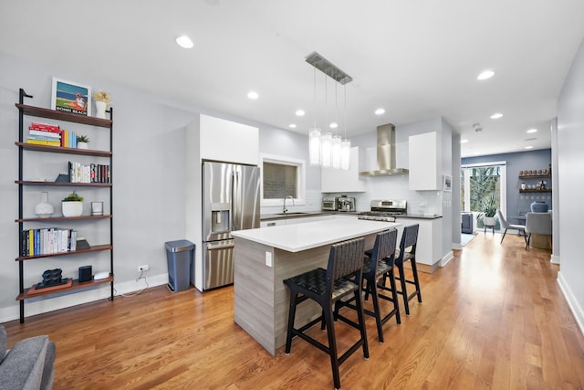 kitchen with white cabinets, a kitchen island, decorative light fixtures, wall chimney range hood, and stainless steel appliances