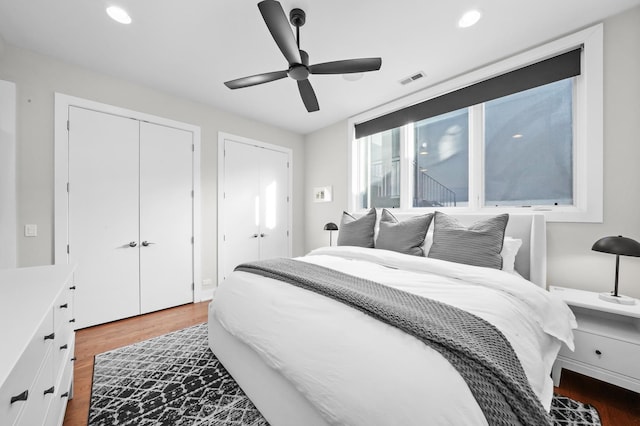 bedroom featuring ceiling fan, dark hardwood / wood-style flooring, and two closets