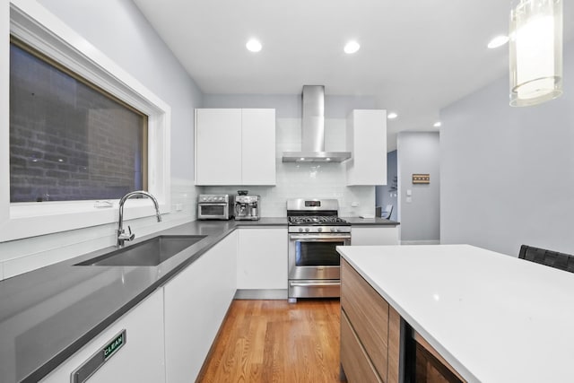 kitchen featuring decorative light fixtures, white cabinetry, wall chimney range hood, sink, and stainless steel range with gas cooktop