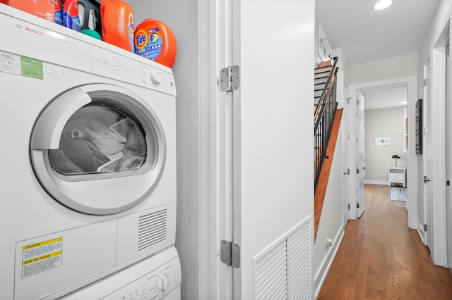 laundry room with hardwood / wood-style floors and stacked washing maching and dryer