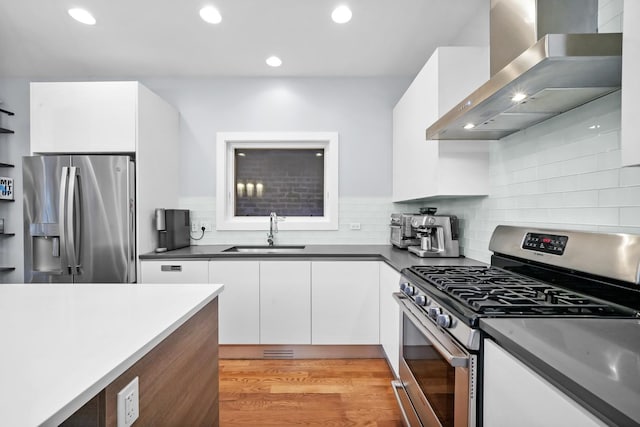 kitchen with appliances with stainless steel finishes, white cabinetry, wall chimney range hood, sink, and light wood-type flooring