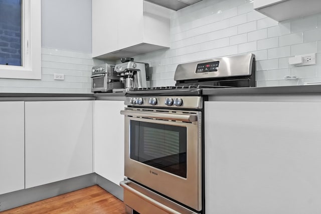 kitchen featuring stainless steel gas range, white cabinetry, light hardwood / wood-style floors, and backsplash