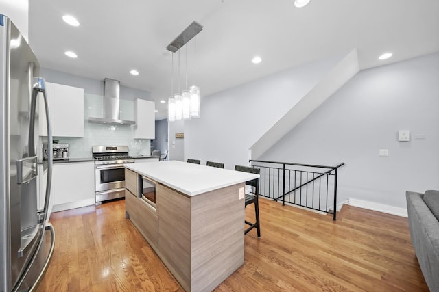 kitchen featuring white cabinetry, stainless steel appliances, pendant lighting, a kitchen island, and wall chimney exhaust hood