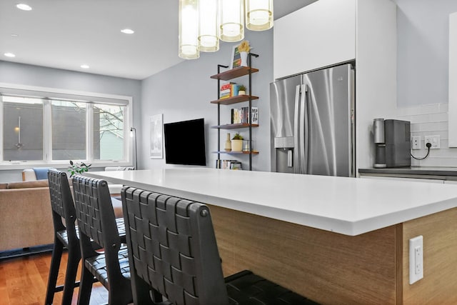 kitchen featuring kitchen peninsula, dark hardwood / wood-style flooring, hanging light fixtures, white cabinets, and stainless steel fridge