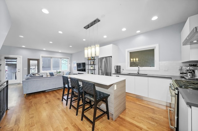 kitchen with a breakfast bar area, stainless steel appliances, decorative light fixtures, white cabinets, and sink