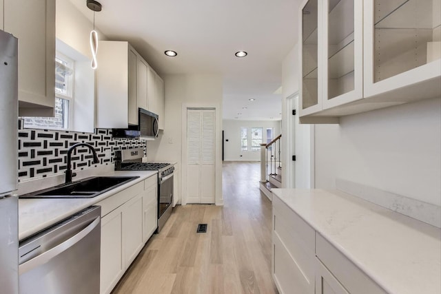 kitchen featuring a sink, light wood finished floors, light countertops, glass insert cabinets, and appliances with stainless steel finishes