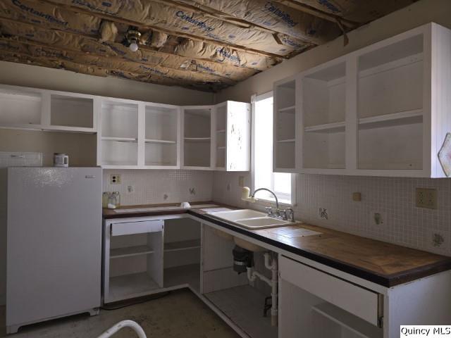 kitchen featuring white cabinetry, butcher block countertops, sink, and white fridge