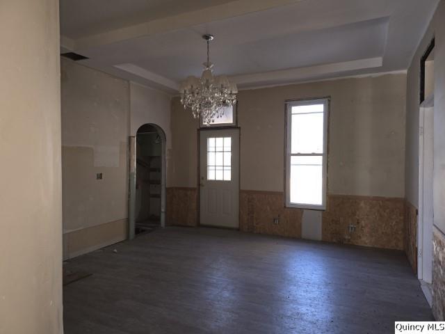 spare room with a tray ceiling, dark wood-type flooring, and a chandelier