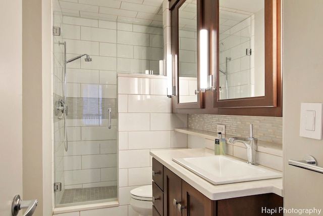 bathroom with backsplash, toilet, a shower with shower door, and vanity