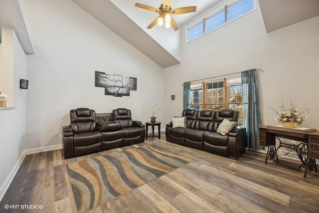 living area featuring a towering ceiling, ceiling fan, baseboards, and wood finished floors