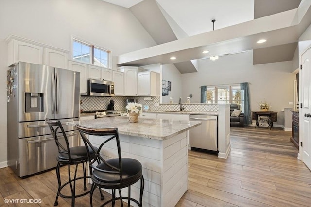 kitchen featuring high vaulted ceiling, a peninsula, a sink, decorative backsplash, and stainless steel appliances