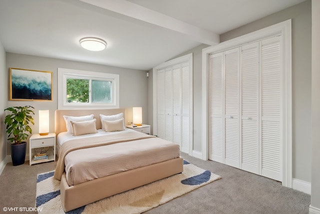 bedroom with light carpet, two closets, and beamed ceiling