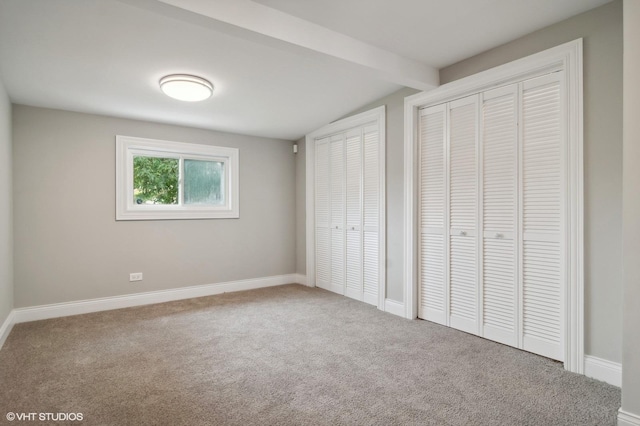 unfurnished bedroom with carpet floors, beam ceiling, and multiple closets