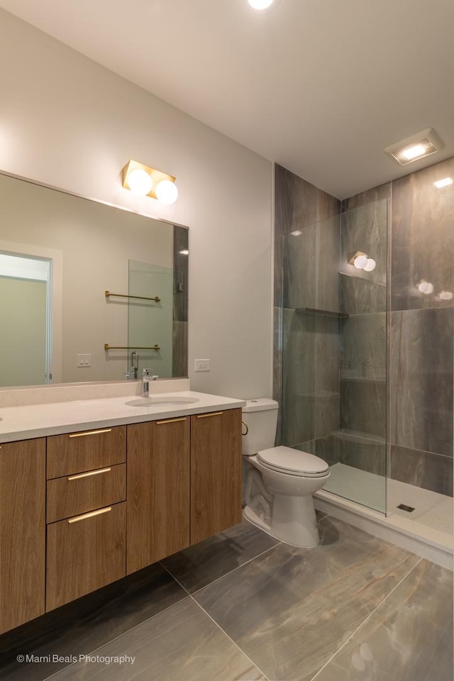 bathroom with toilet, vanity, a tile shower, and tile patterned flooring