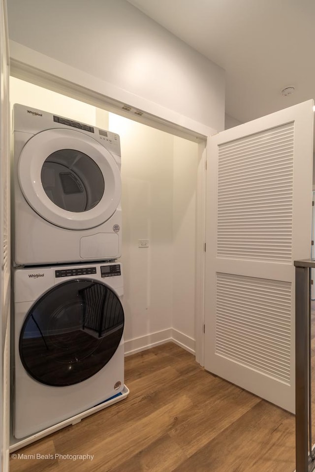 clothes washing area with wood-type flooring and stacked washer / drying machine