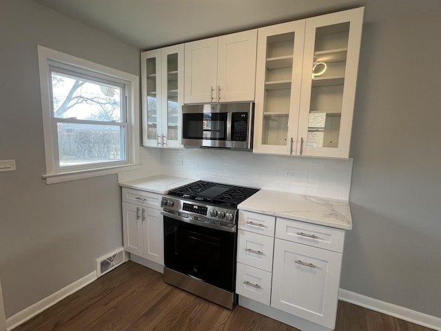 kitchen featuring appliances with stainless steel finishes, white cabinetry, backsplash, light stone counters, and dark hardwood / wood-style flooring