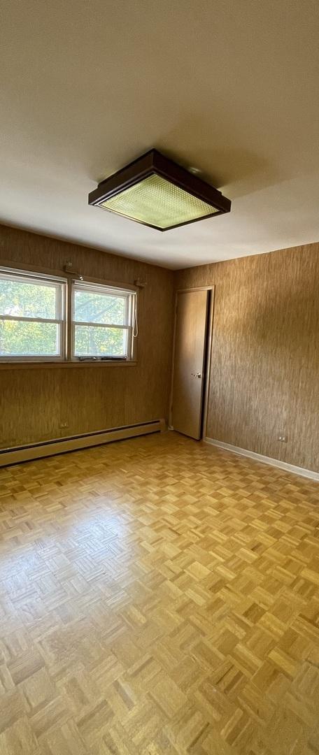 empty room featuring light parquet flooring, wood walls, and a baseboard radiator