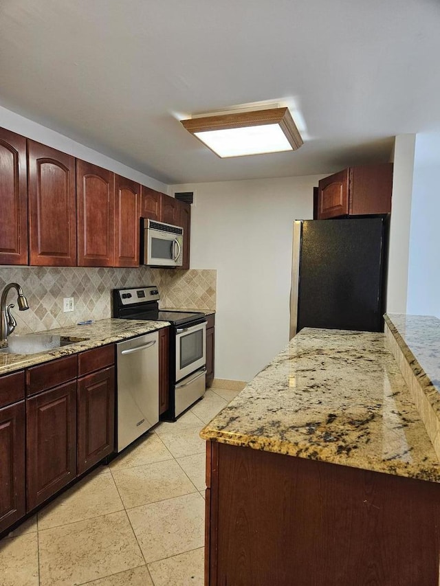 kitchen featuring light tile patterned floors, light stone countertops, appliances with stainless steel finishes, and sink