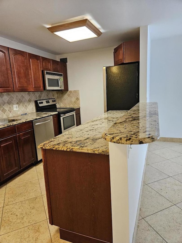 kitchen with light tile patterned floors, decorative backsplash, light stone counters, and stainless steel appliances