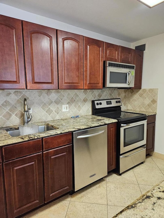 kitchen with appliances with stainless steel finishes, decorative backsplash, light tile patterned flooring, light stone countertops, and sink