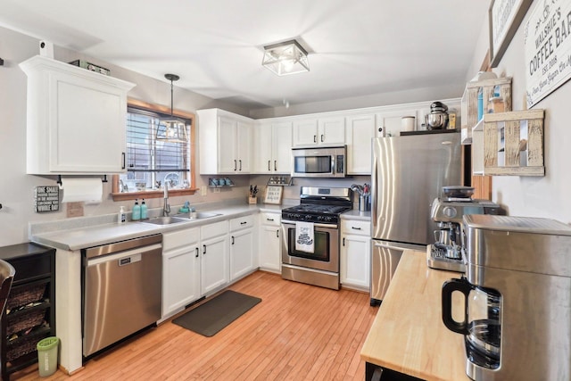 kitchen with white cabinets, hanging light fixtures, appliances with stainless steel finishes, and light wood-type flooring