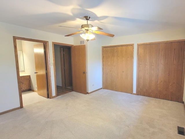 unfurnished bedroom featuring ceiling fan, light colored carpet, two closets, and ensuite bathroom