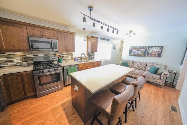 kitchen with appliances with stainless steel finishes, tasteful backsplash, light hardwood / wood-style floors, rail lighting, and hanging light fixtures