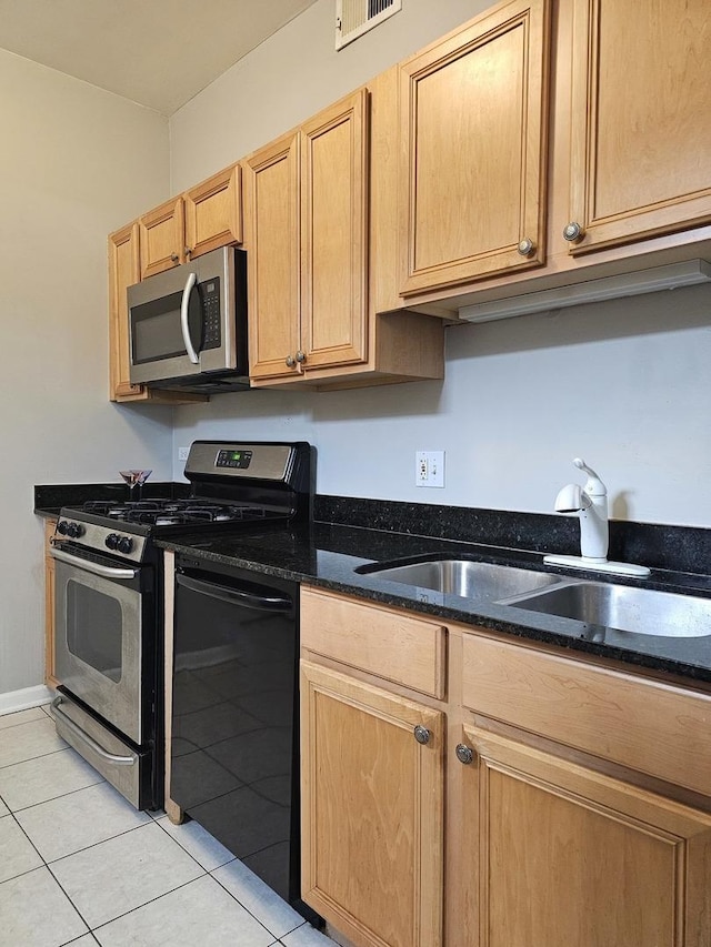 kitchen with appliances with stainless steel finishes, light brown cabinets, light tile patterned flooring, dark stone countertops, and sink