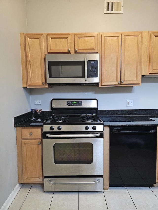 kitchen with light brown cabinetry, appliances with stainless steel finishes, light tile patterned flooring, and dark stone countertops