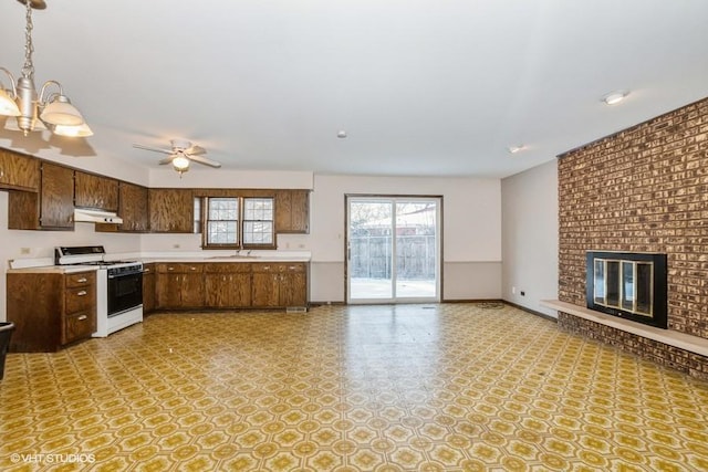 kitchen with sink, gas range gas stove, hanging light fixtures, a brick fireplace, and ceiling fan with notable chandelier