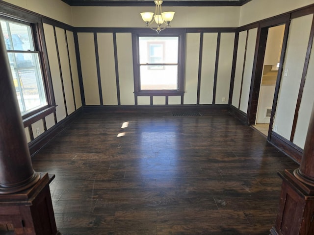 empty room featuring dark hardwood / wood-style floors, ornate columns, and a chandelier