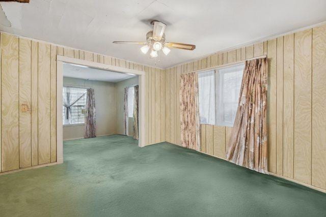 empty room featuring ceiling fan, carpet, and wooden walls