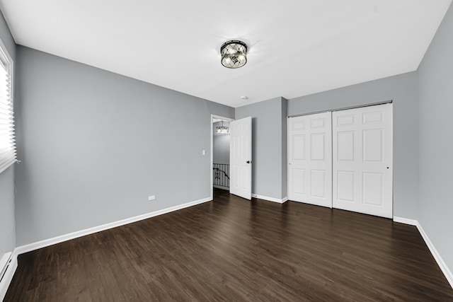 unfurnished bedroom featuring dark wood-type flooring, a closet, and a baseboard heating unit