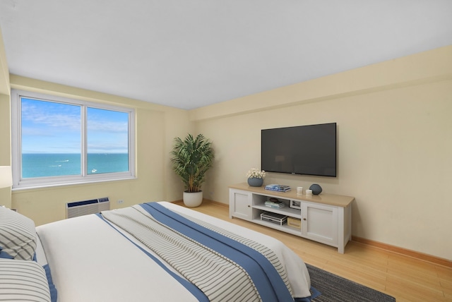 bedroom with a wall mounted AC, light hardwood / wood-style flooring, and a water view