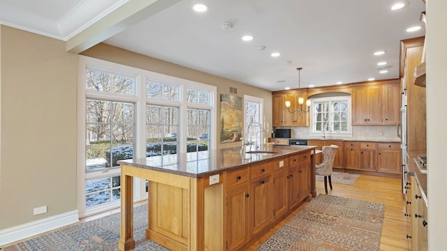 kitchen with dark stone countertops, a center island with sink, sink, hanging light fixtures, and a kitchen breakfast bar