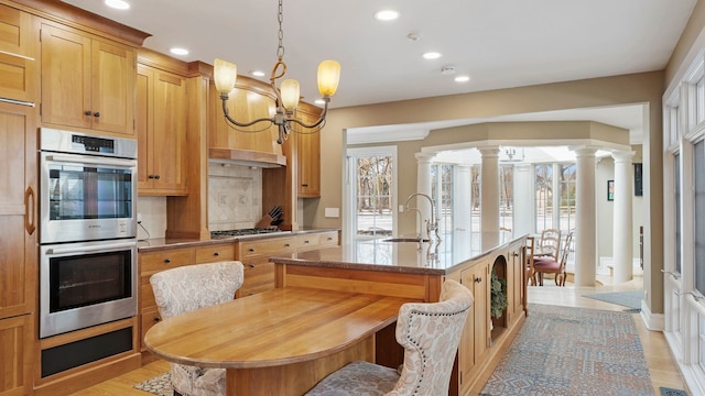 kitchen with a notable chandelier, sink, appliances with stainless steel finishes, an island with sink, and decorative columns