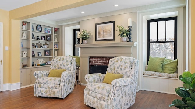 sitting room with built in features, a brick fireplace, and dark hardwood / wood-style flooring